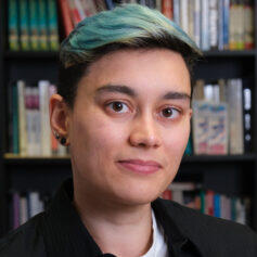 Ishani Dugar Person with medium skin and short dark hair died teal blue looks straight at camera with bookshelves in the background